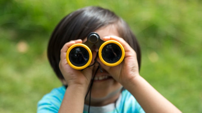 A child looks through yellow binoculars directly at the camera with a big smile on his face.